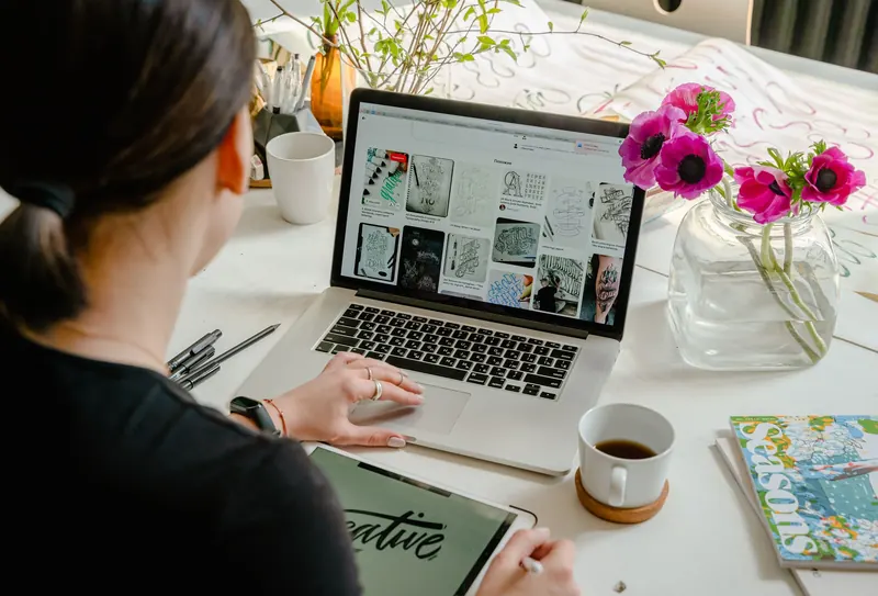 Frau entwirft einen Schriftzug am Laptop, daneben Blumen und Kaffee